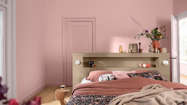 Calm bedroom with blush-pink walls, a made bed, and a decorative shelf above the headboard.