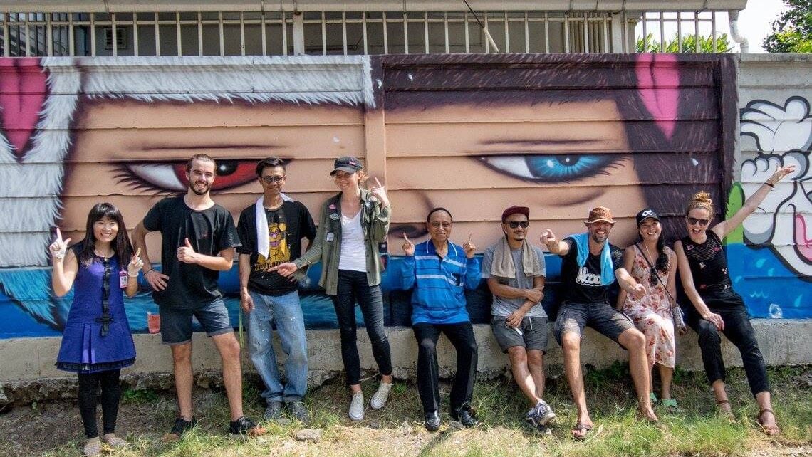 Group of people posing in front of a colourful graffiti mural with a large painted eye.