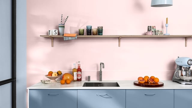 Bright kitchen with pastel blue cabinets, pink wall, sink, and orange fruit on the worktop