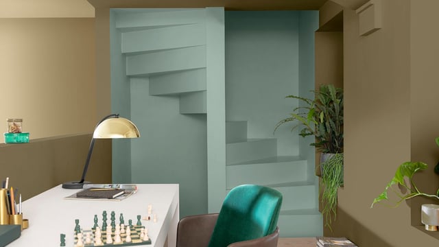 Modern home office with a white desk, chess pieces, a turquoise chair, and green plants.