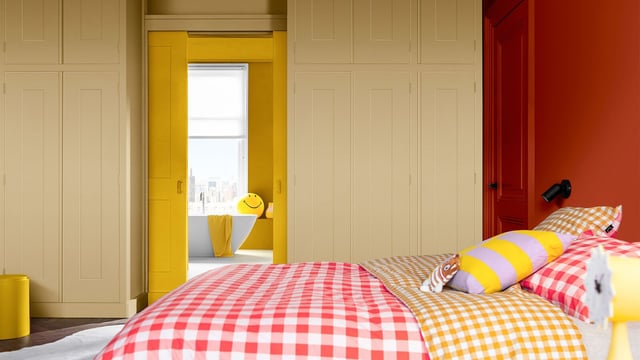 Bright bedroom with an open yellow doorway, plaid bedding, and patterned pillows.