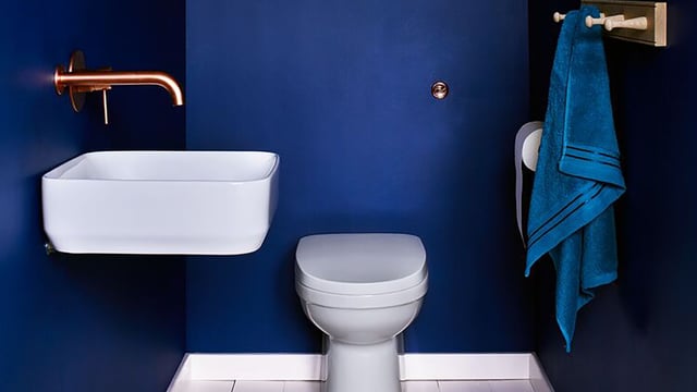 Modern bathroom with white sink, toilet, blue wall, copper faucet, and hanging blue towel.