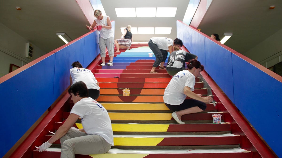 Several people paint a school staircase, with bright steps in blue, red and yellow.