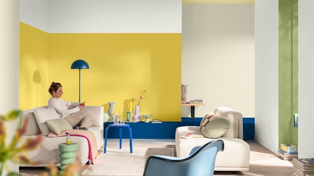 Modern living room with beige chairs, a blue side table, and a striking yellow accent wall