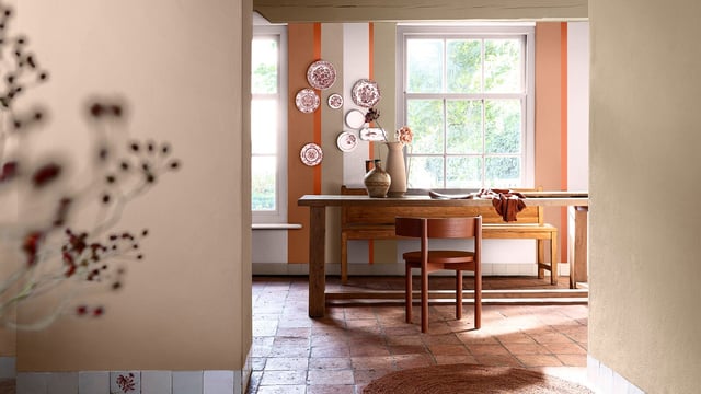 Bright kitchen with a wooden table, chairs, vases, and wall decorations near a large window.