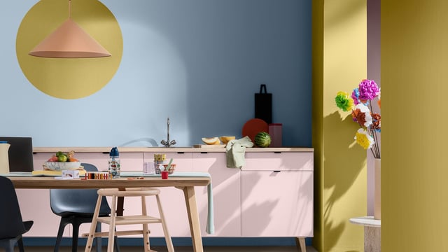 Bright kitchen with blue and yellow walls, white cabinets, stools, and a vase of flowers.