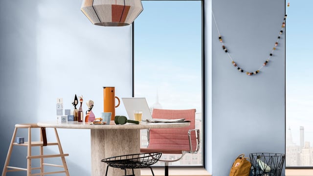 Bright home office with blue walls, desk, laptop, pink chair, and skyline view through windows.