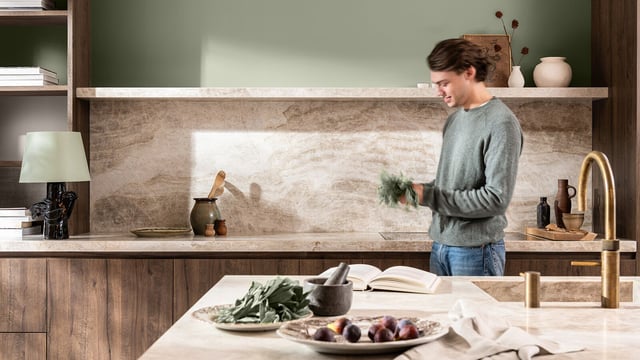 Man standing in a modern kitchen, holding a bunch of fresh herbs over the countertop