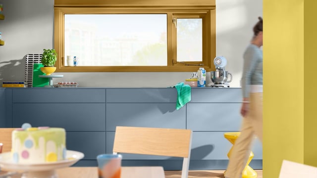 Bright kitchen with blue cabinets, a sink, and dishes; a person walks past.