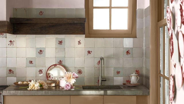 Bright kitchen with patterned tiles behind the sink, a window, and flowers on the countertop