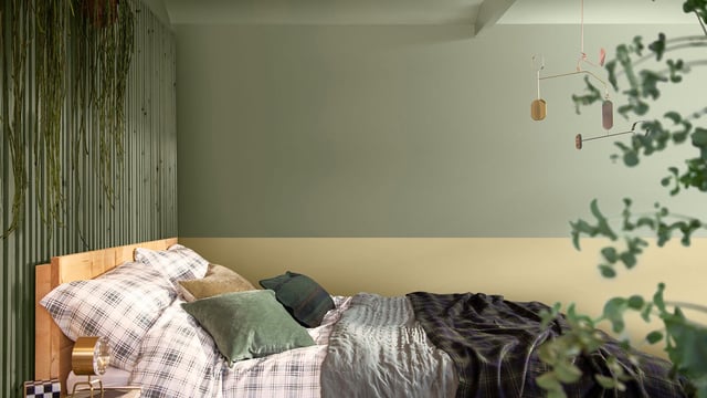 Sunlit bedroom with an unmade bed, green pillows, and hanging pendant lights; plants in the foreground.