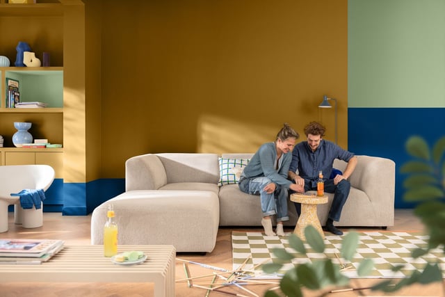 Modern living room with a light gray sofa and blue-yellow accents; a couple sits and talks together.