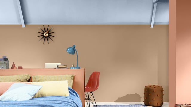 Bright bedroom with a low bed, orange wall, blue desk lamp, and modern chair and pouffe.