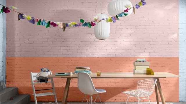 Bright home office with desk, chairs, shelves and hanging paper decorations on a brick wall.