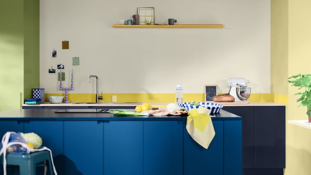 Blue kitchen cabinets with a light countertop, shelf, and cookware in a bright, modern room.