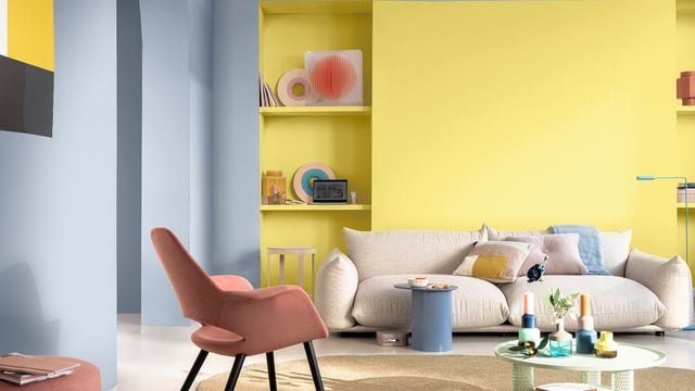 Bright living room with yellow feature wall, beige sofa, side tables, and decorative shelves