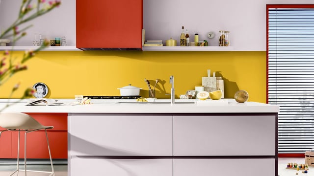 Stylish kitchen with a yellow wall, white countertop, and red-orange cabinets.