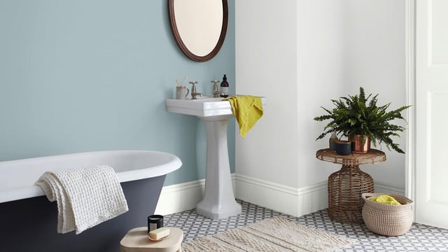 Bright bathroom with freestanding bath, white pedestal sink, grey tiles, potted plant and yellow towels