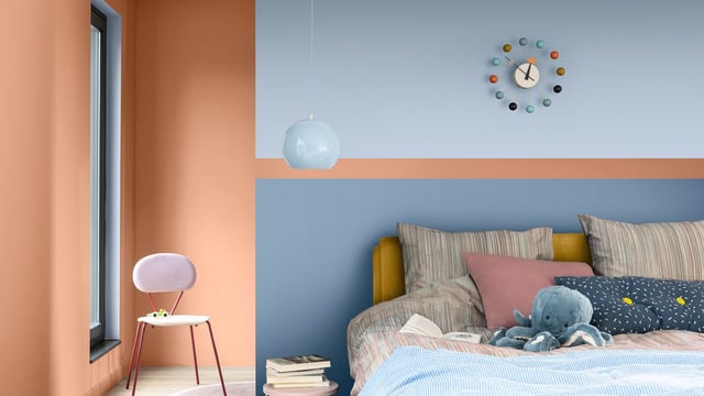 Bright bedroom corner with double bed, cushions and teddy, wall clock, and a glowing bedside table lamp.