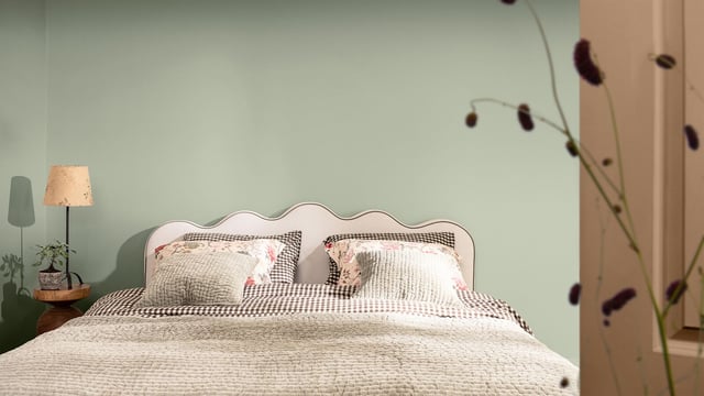 Cozy bedroom with a patterned bed, two pillows, soft lighting, and a sage green wall
