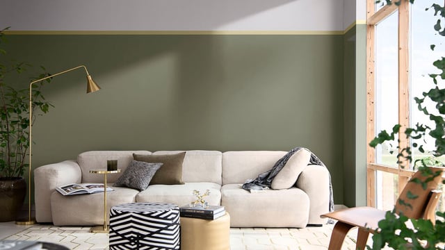 Bright living room with a cream sofa, green wall, and large window with leafy plants.