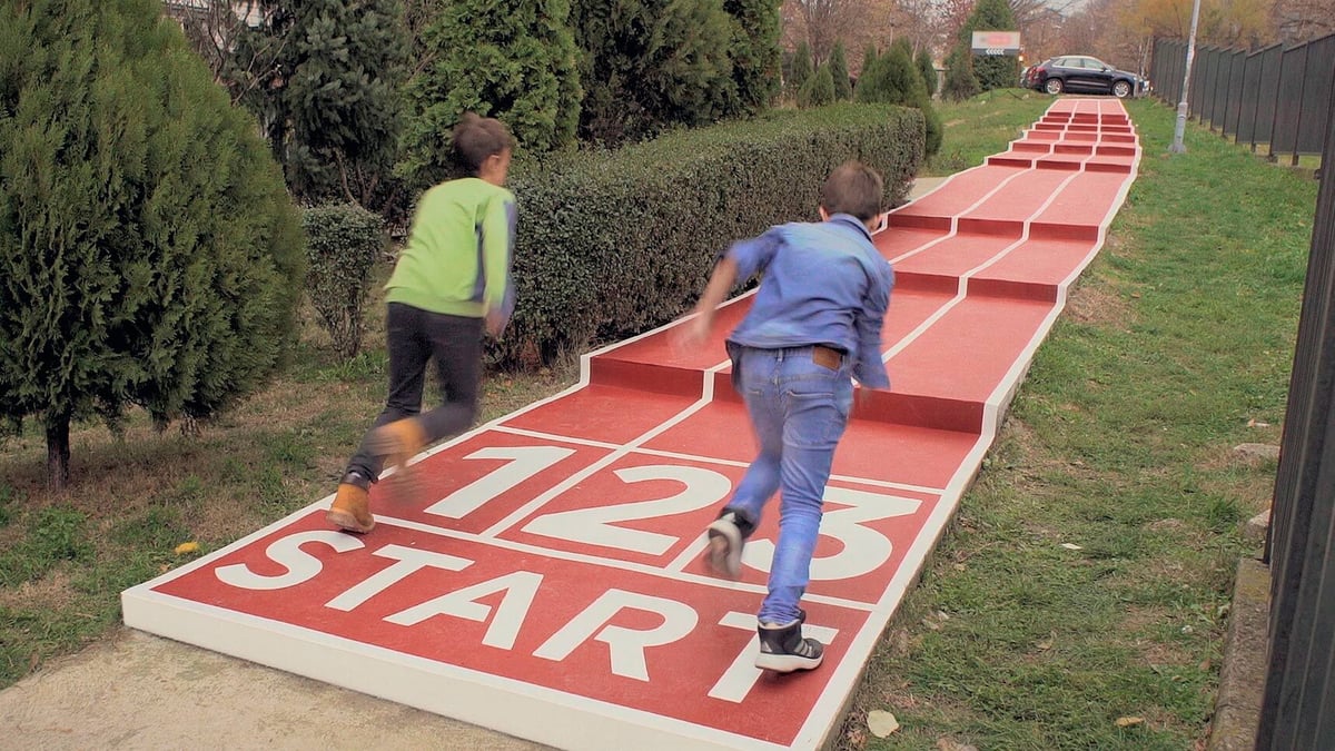 Children play on a large outdoor red hopscotch mat with “START” lettering