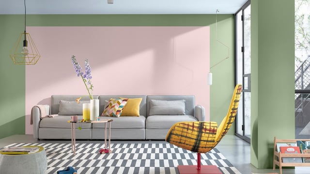 Bright living room with green walls, sofa, colourful cushions, patterned rug, and hanging pendant light