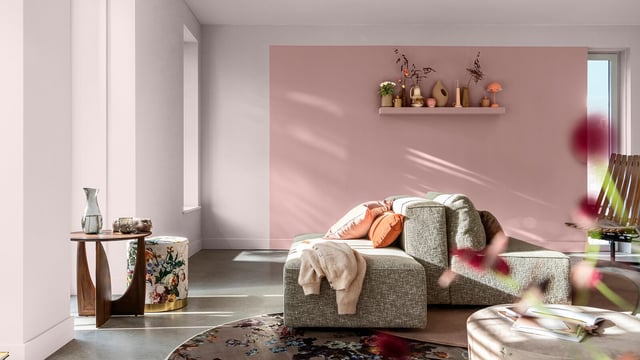 Modern living room with a gray sofa, blankets, and decorative items on a shelf against a warm violet wall